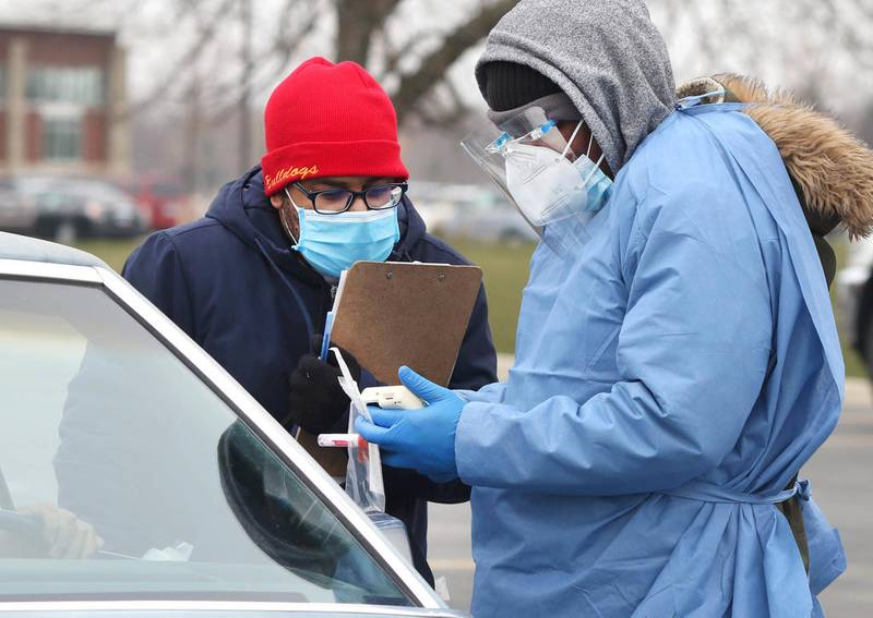 Enrique Jones, (left) an HR Support site manager, and Adebayo Adeniyan, a phlebotomist from HR Support, take a sample from a patron on a cold Tuesday afternoon at the COVID-19 testing location in the parking lot at the Kishwaukee Family YMCA in Sycamore.
