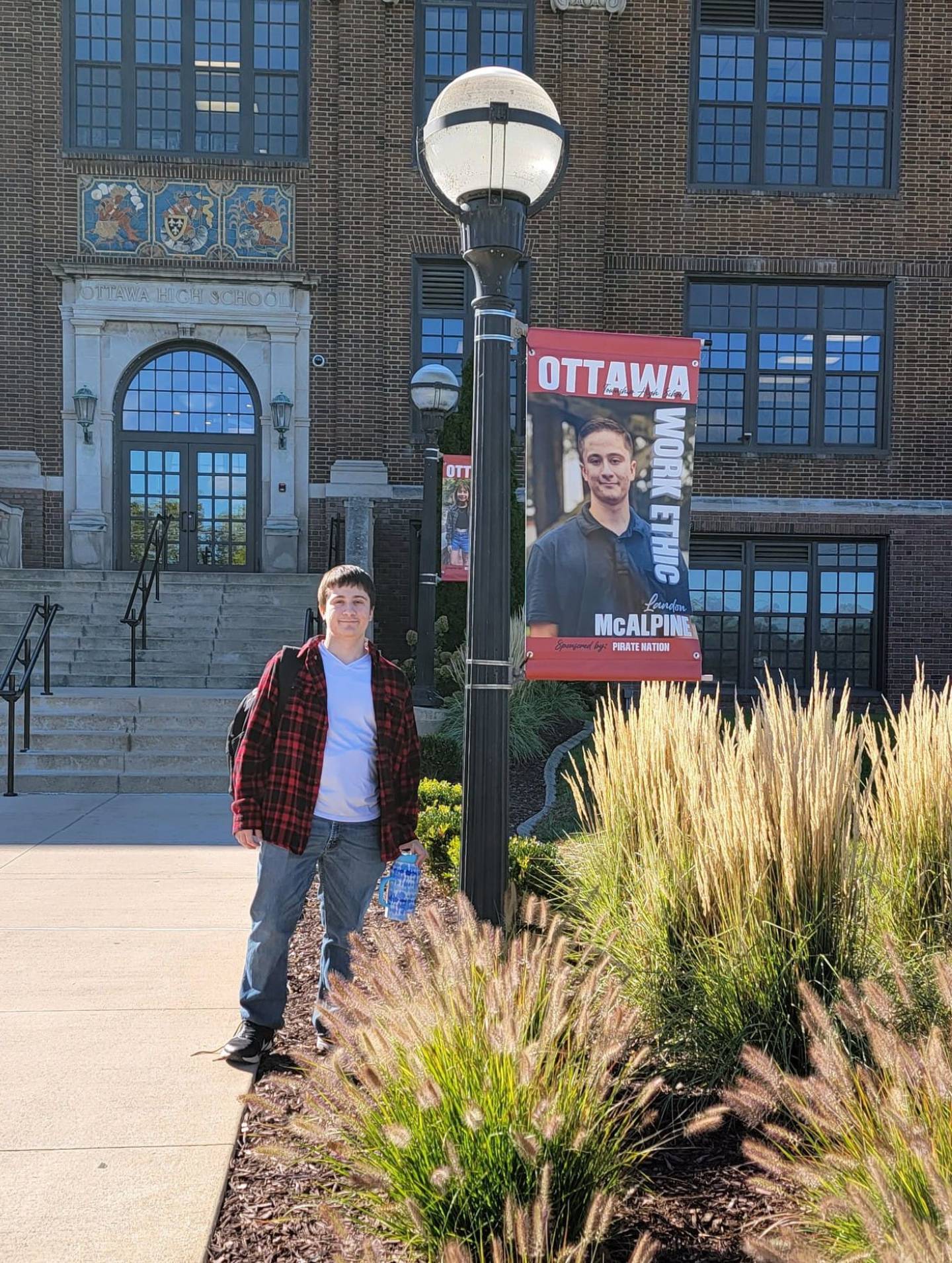 Landon McAlpine takes a photo with a banner made for him outside of Ottawa High School. McAlpine died Dec. 26, 2022.
