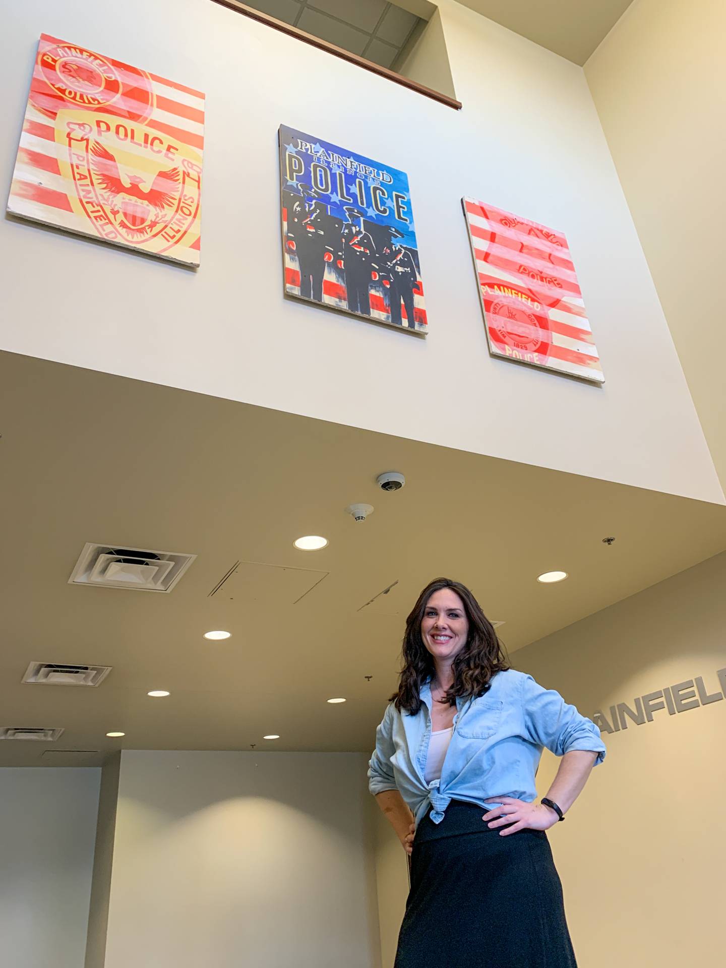 Plainfield High School-Central Campus art teacher Lindsey Brown stands below her artwork in the Plainfield Police Department's Branch Court lobby. Brown designed and painted the three-panel mural at the department's request.