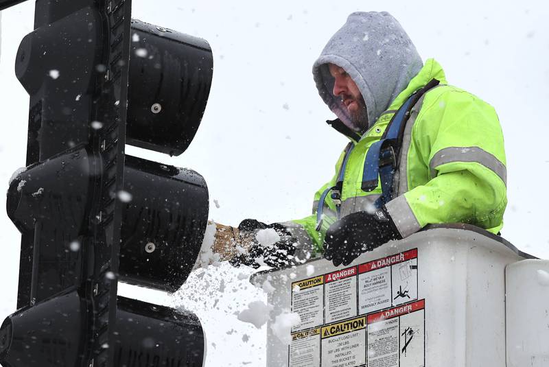 Kyle Krenz, an electrician with DeKalb Public Works, removes snow that has accumulated on the stoplights at the intersection of Lincoln Highway and Fourth Street Tuesday, Jan. 9, 2024, in DeKalb. Snow is expected to continue throughout the day with 7 to 10 inches of snow expected.