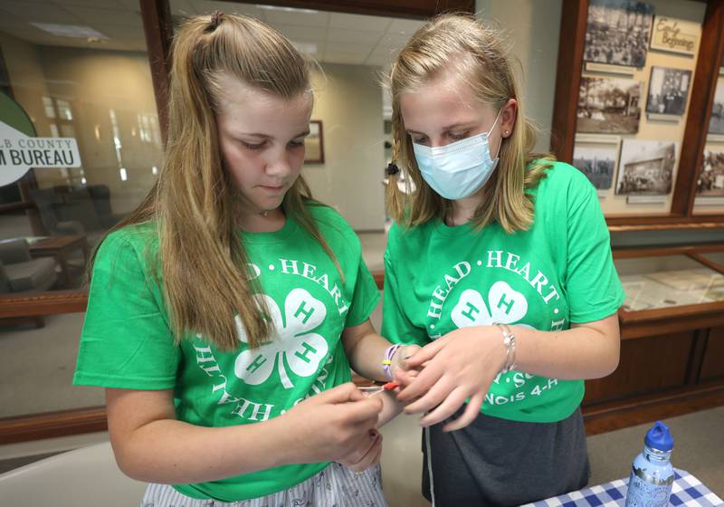 Maggie Kushnick, (left) 11, from Sycamore, gets some help making a bee buzzer noise maker from her sister Ella, 13, Thursday, July 14, 2022, at the 4-H General Project Show at the DeKalb County Farm Bureau in Sycamore. Both were volunteers with 4-H, helping to staff a station at the show.