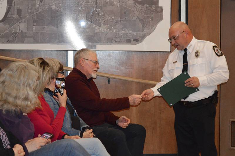 Rock Falls Police Chief David Pilgrim hands Tim Isaac, of Rockford, a challenge coin during the March 19, 2024, Rock Falls City Council meeting. Pilgrim and others were honored at the meeting for saving Isaac's life Feb. 14, 2024, after Isaac had a medical emergency while driving.