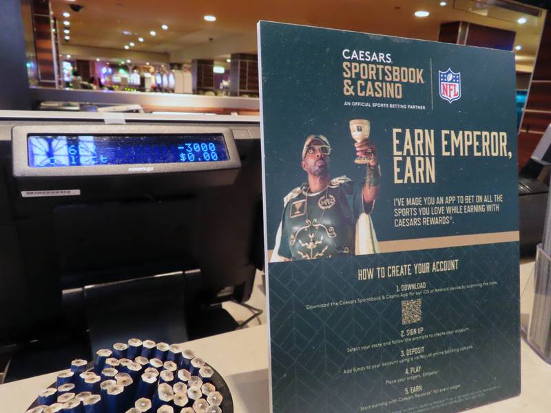 A sign bearing an advertisement for Caesars Entertainment's sports betting operation sits near a sports betting terminal in the sports betting lounge at the Tropicana casino in Atlantic City N.J. on Thursday, May 12, 2022. Caesars is one of the most frequent advertisers of sports betting in the United States, where gamblers have wagered over $125 billion on sports with legal betting outlets in the four years since the U.S. Supreme Court cleared the way for all 50 states to offer legal sports betting. (AP Photo/Wayne Parry)