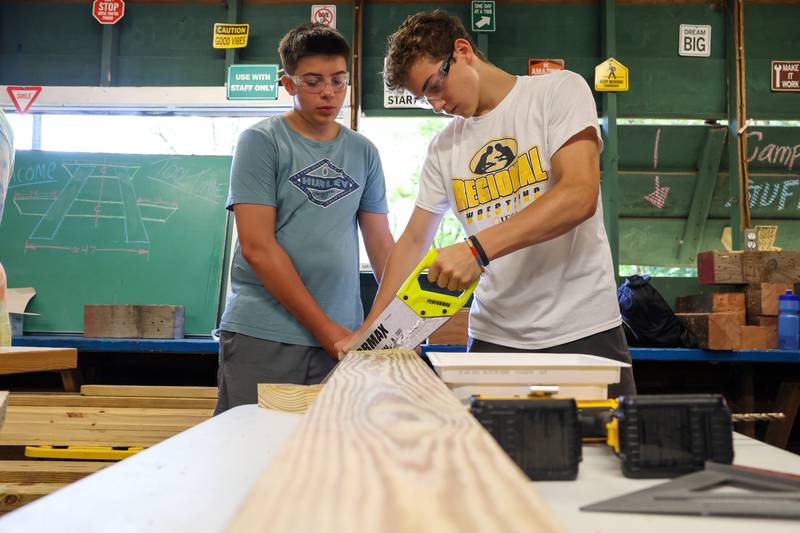 Jax Abrassart, left, 13, of Bradley, helps steady a wooden board as Alex Vincic, 14, of Lake Villa, cuts it to length with a saw during Tool Time at Camp Shaw-Waw-Nas-See on Wednesday, July 16, 2025.