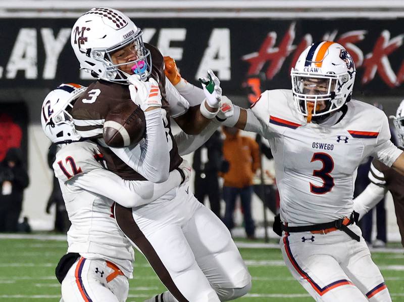 Mount Carmel's Marshaun Thornton goes up between Oswego's Jake Walsh (left) and Devin Mata to try and make a catch Wednesday, Dec. 3, 2025, during their IHSA Class 8A state chamionship game in Huskie Stadium at Northern Illinois University in DeKalb.