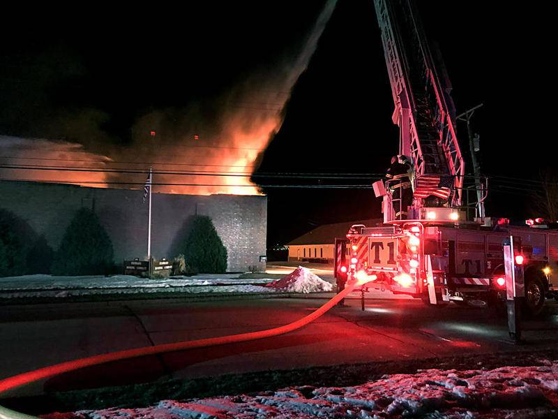 Firefighters spray water from above the flames Friday at 1100 S. Seventh St. in DeKalb after the Standard Roofing Co. building caught fire.