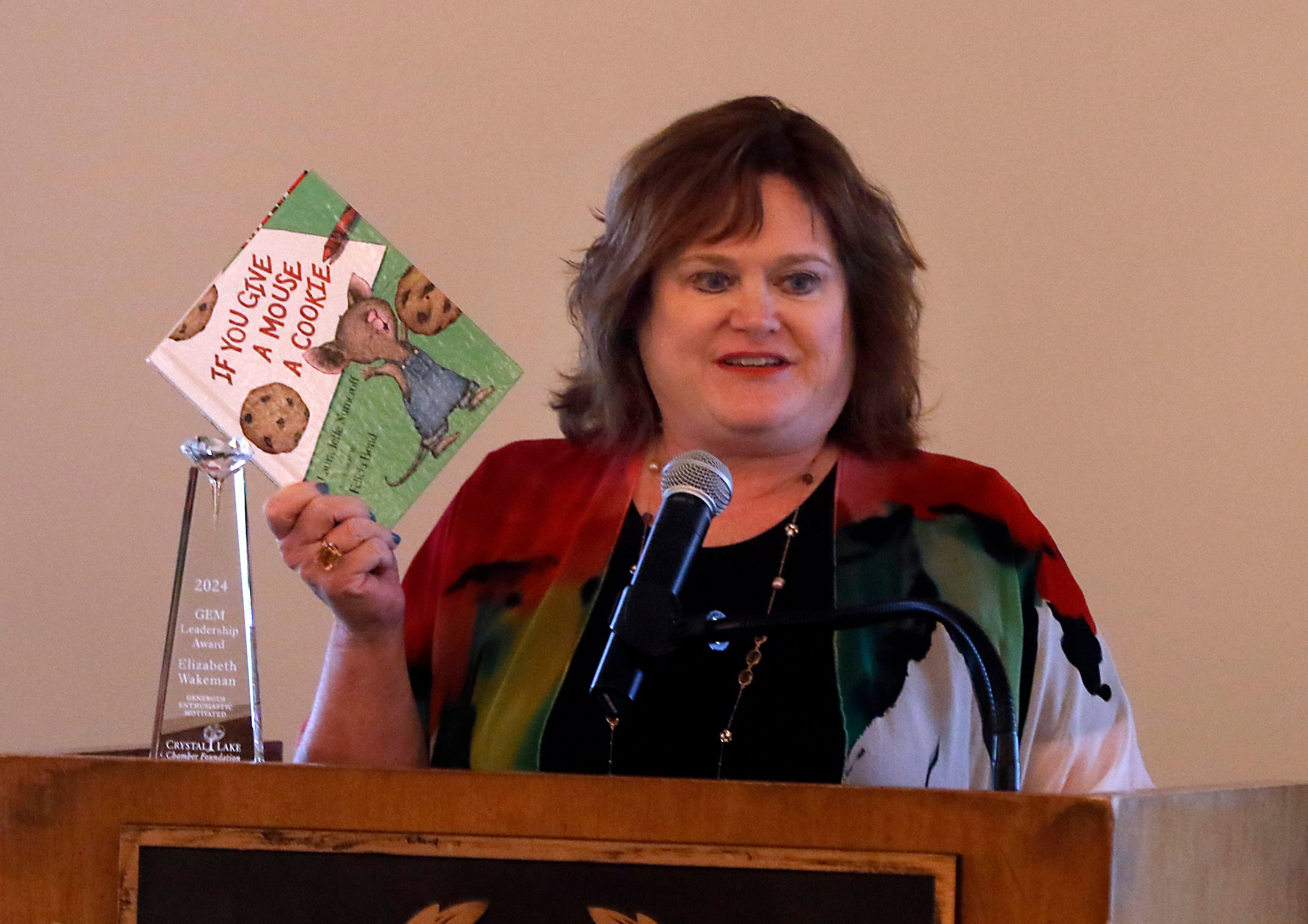 GEM award winner Elizabeth Felt Wakeman holds up the book “If You Give A Mouse a Cookie” during her speech at the Crystal Lake Chamber Foundation's 11th Annual GEM Awards Leadership Celebration on April 18, 2024, where she was an honoree. 