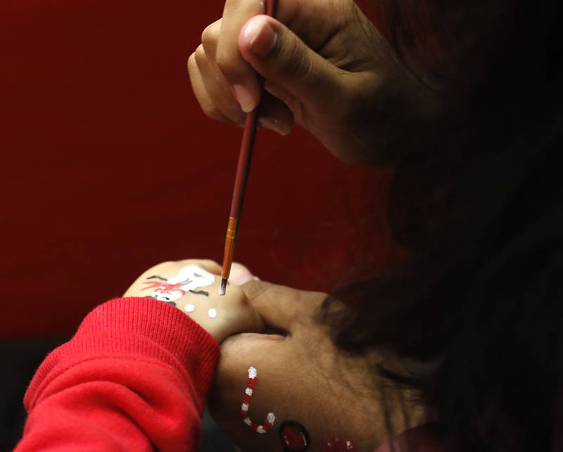 Volunteer Neha Gopal paints a snowman on the hand of Valerie Silva, 4, of Huntley, Friday, Dec. 2, 2022, during the Very Merry Huntley Holiday Open House at the Huntley Area Public Library. The event featured musical entertainment by Andy Huber, reindeer, Santa, a scavenger hunt, face painting, and a snowball toss.
