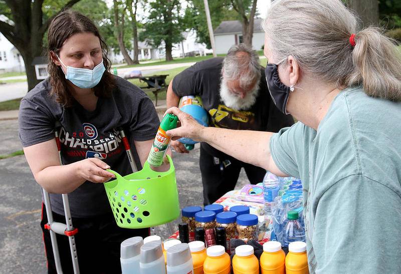 Theresa Popelka (left) is handed a bottle of bug spray from Sue Rekenthaler of Richmond (right) as Bill Urban looks at water bottles July 21, 2020, at the First United Methodist Church of McHenry in McHenry. Compassion for Campers is hosting a fundraising event on Wednesday, Aug. 30, to fund continuing distribution of supplies.