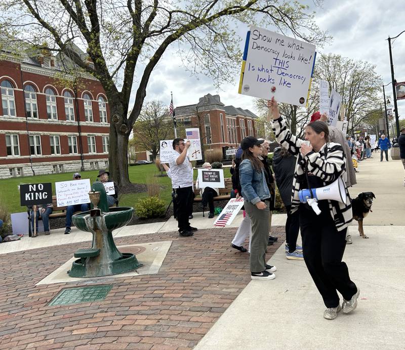 Jan Buttron of Chana, one of the Hands Off rally organizers, carries a sign while she speaks with a megaphone during the rally on Saturday, April 19, 2025 around the historic Ogle County Courthouse in Oregon.