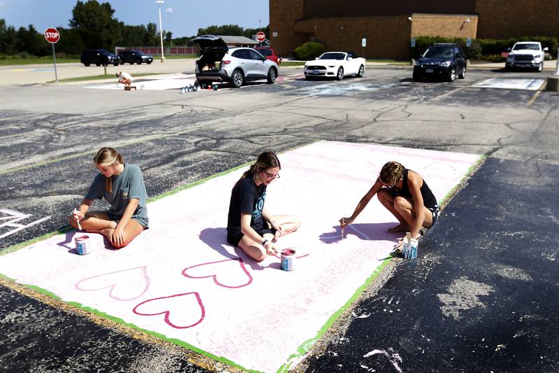 Juniors Holly Zabroski, Tessa Weber, and Tessa’s sister, graduate Emma Weber, paint hearts on Tuesday, Aug. 13, 2024, while helping to paint Tessa Weber’s parking spot at Marion Central Catholic High School in Woodstock.