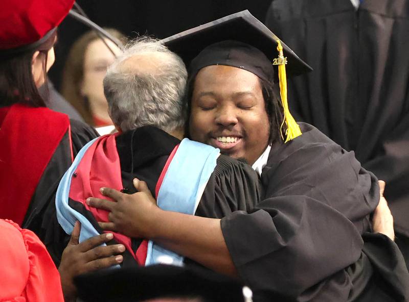A Northern Illinois University graduate hugs a member of the faculty as he receives his diploma during the first of two undergraduate commencement ceremonies Saturday, May 11, 2024, in the Convocation Center at NIU in DeKalb.