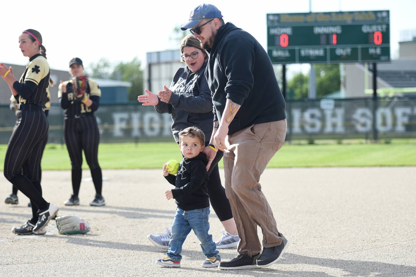 Kyler Medina, 2, of Bradley, walks onto the Bishop McNamara softball field with his parents, Paige and Travis, before throwing out the ceremonial first pitch ahead of the All-City softball game between Bishop McNamara and Bradley-Bourbonnais. The two schools raised money for Medina, who recently began cancer treatment, and his family.
