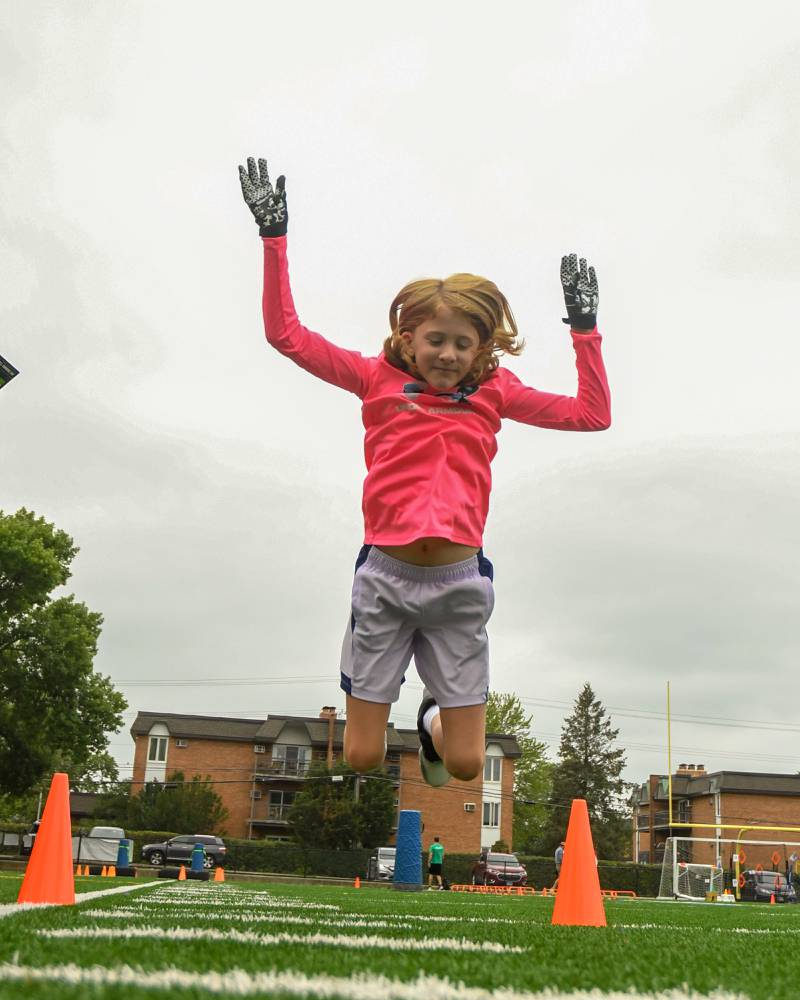 Evelyn Dedo, 7, of Darien sees how far she can jump during a standing long jump portion of the NFL Youth Flag Football Combine Day held at Doerhoefer Park in Downers Grove on Sunday Aug. 6, 2023.