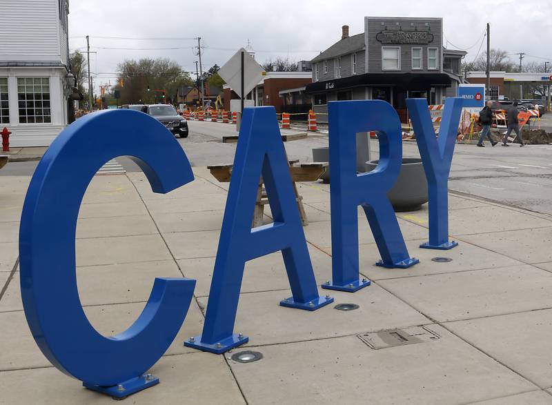 People cross the street near the Cary sign at the intersection of West Main Street and Spring Street in Cary on Tuesday, April 25, 2023. The village of Cary is considering a new tax increment financing district in its downtown corridor to help spur new development in the oldest part of its town.