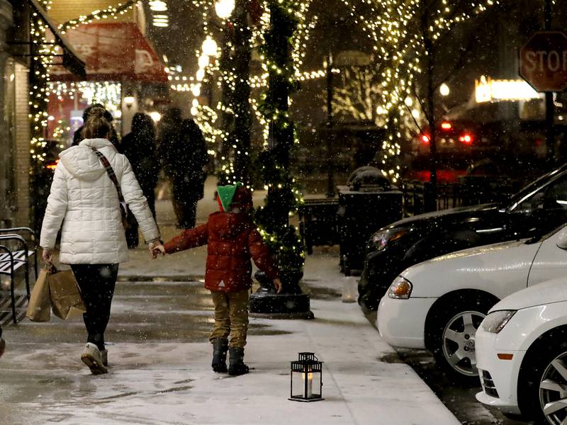 A child holds his mothers hand as they travel between shops during Crystal Lake's Luminary Nights on Thursday, Dec. 19, 2024, in downtown Crystal Lake. The snowy night featured sidewalks lite luminaries, holiday shopping and a visit to the Santa House.