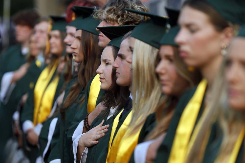 Students stand for the National Anthem during the Glenbard West commencement ceremony Thursday May 18, 2023 on Duchon Field in Glen Ellyn.