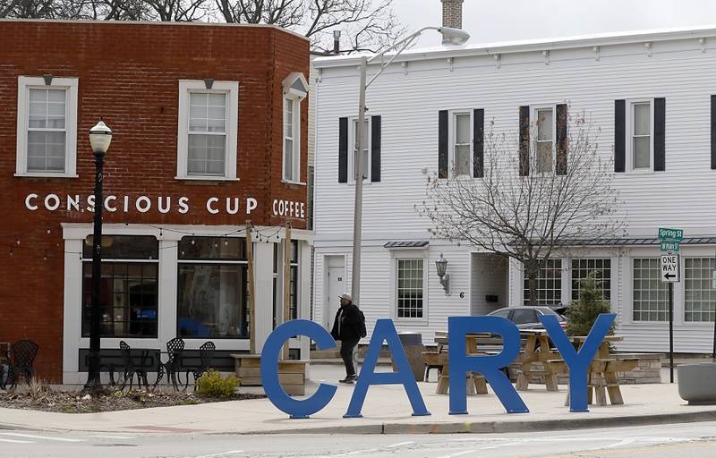 A man walks past the Cary sign in near the intersection of West Main Street and Spring Street in Cary on Tuesday, April 25, 2023. The Village of Cary is considering a new tax increment financing district in its downtown corridor to help spur new development in the oldest part of its town.