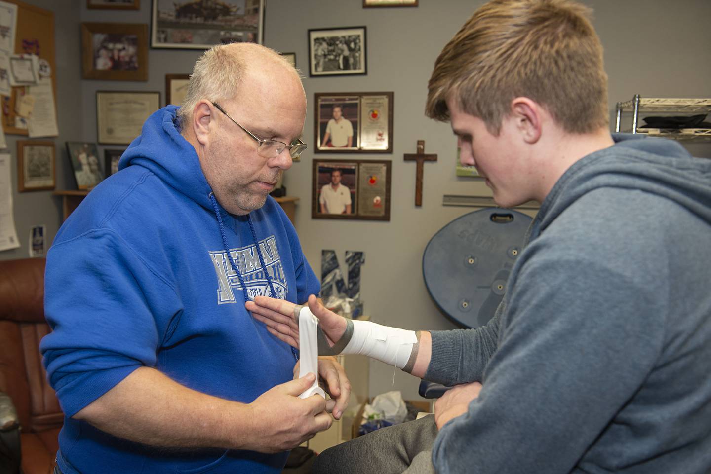 Newman athletic trainer Andy Accardi wraps up son Christopher's wrist before practice at the school.