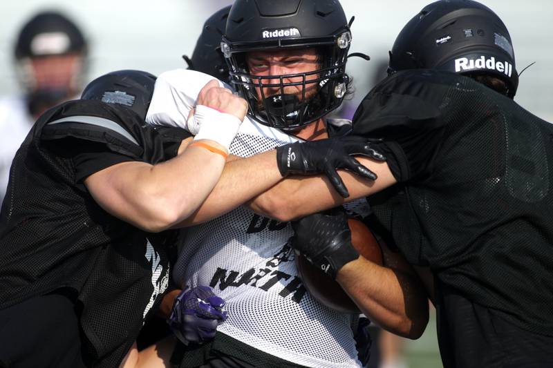 Downers Grove North’s Robby Farrington gets squeezed by his teammate defenders during a practice at the school on Tuesday, Aug. 15, 2023.