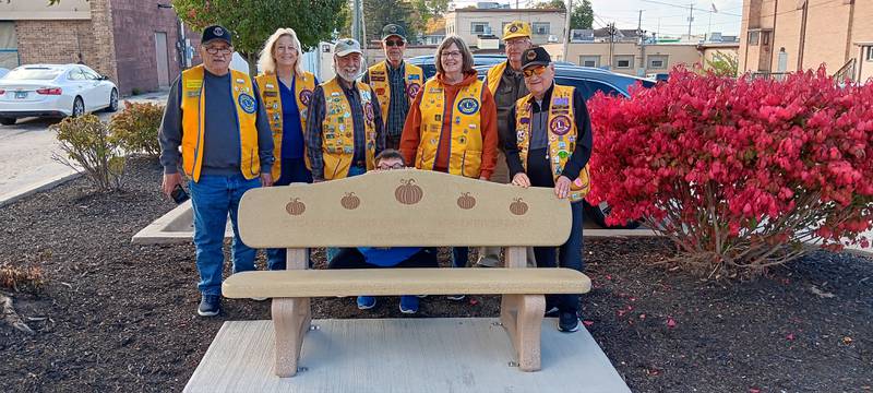 (From left) Sycamore Lions John Polichnowski, Kathy Smith, Jerome Perez, Ed Kuhn, President Kathleen Weisser, Jerry Malmassari and Tom Moline pose in front of the Sycamore Lions Club bench Tuesday, Oct. 24, 2023 on East State Street in Sycamore. Doty and Sons and The Sycamore Lions Club are each celebrating a 75-year anniversary. The bench was installed in that honor.
