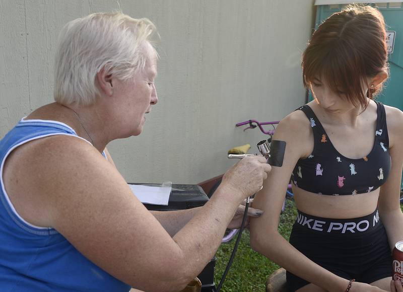 Gianna Foster has a design airbrushed on her arm Tuesday, Aug. 1, 2023, by Kathy Kocher at the Marseilles Pool during National Night Out.