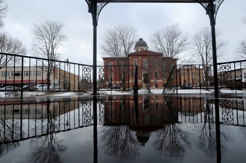 The Old Courthouse and Jail is reflected in melting snow Sunday afternoon, Feb. 28, 2021, in the Historic Woodstock Square as people enjoy a bit of warmer weather do doe some outside activities.