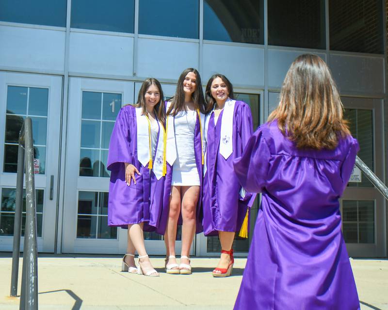 Downers Grove North seniors Veronica Latosha, Megan Campbell and Nevi Marinakos pose in front of the school as Emerson Lewis takes a photo on Sunday May 19, 2024, before the start of the graduation 
ceremony held at Downers Grove North High School.