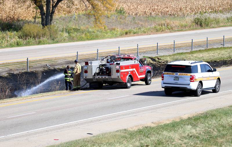 Utica firefighters extinguish a brushfire in the median as an Illinois State Police vehicle passes by on Wednesday, Oct. 9, 2024 near mile post 65 in Bureau County.