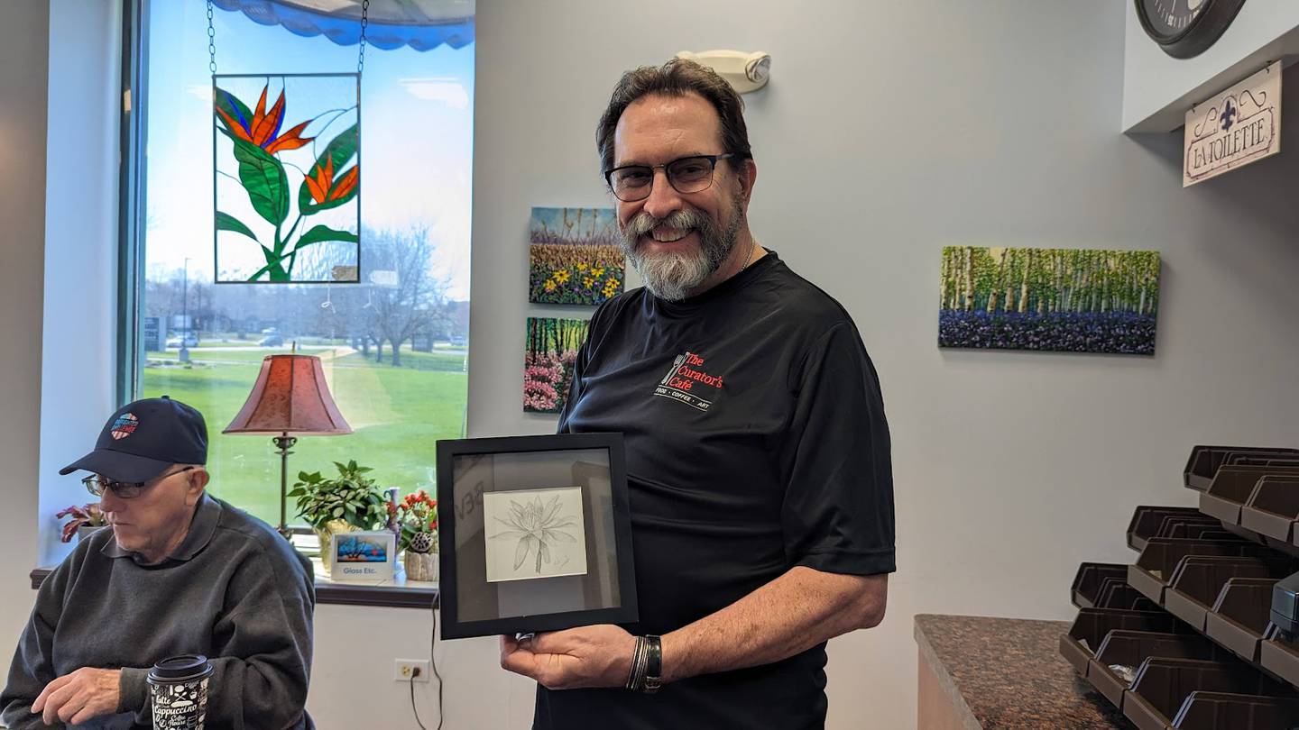 Tom Grotovsky, owner of The curator's Cafe in Joliet (right) holds up an art piece  that Ted Overcash of Joliet (left) created with a sterling silver pencil.