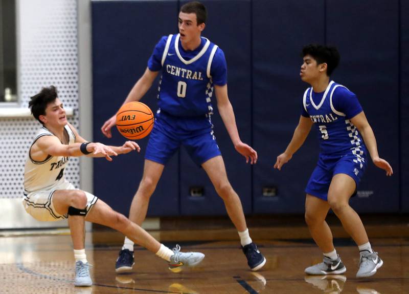 Cary-Grove's Dylan Dumele passes the ball as he falls to the court while be defended by Burlington Central's Patrick Magan (center) and Cedric Ceniza during a Fox Valley Conference  boys basketball game on Wednesday Jan. 7,  2026, at Cary-Grove High School, in Cary.