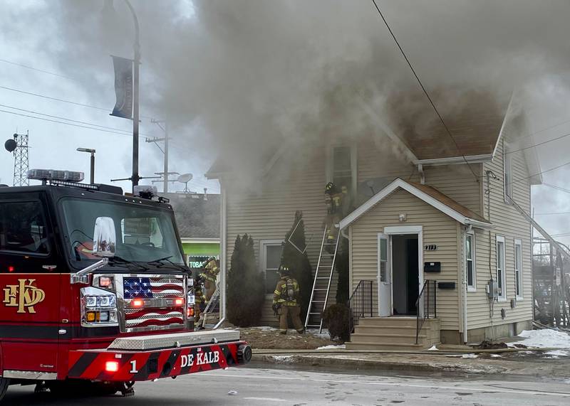 A firefighter on a ladder works to break the upstairs window to a two-story duplex to get water into the structure on Saturday, Jan. 24, 2026, at Seventh Street and East Lincoln Highway in downtown DeKalb. Fire Chief Luke Howieson said the rampant flames spread too quickly into the walls for it to be safe for firefighters to remain in the building.