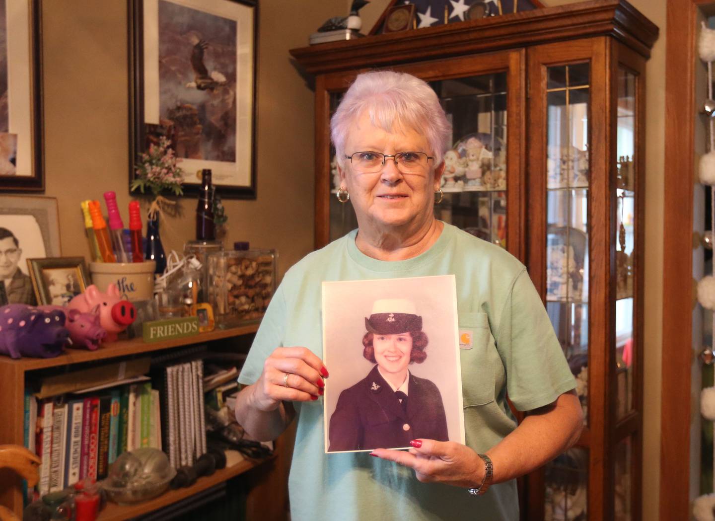 Navy Veteran Kathy Lawyer, poses in her home with a photo of her in the service on Wednesday, Sept. 3, 2025 in Oglesby.