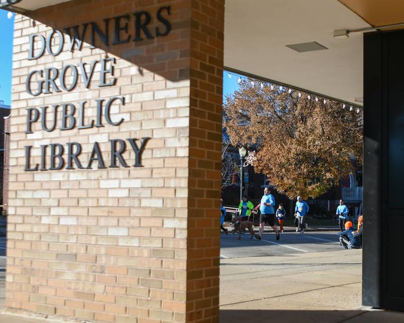 Participants run past the Downers Grove Public library during the Grove Express 5k race in downtown Downers Grove on Thursday Nov. 23, 2023.