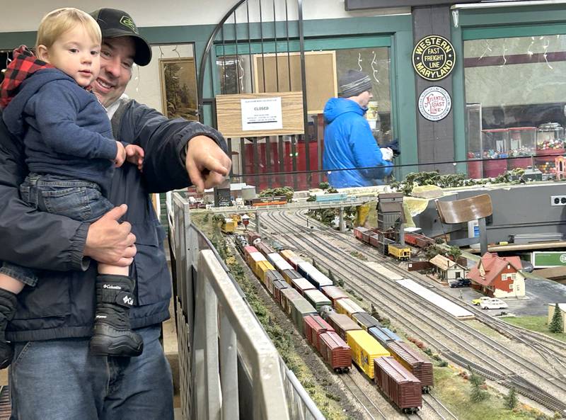 Jeff Schrade and his son, Korey, 9 months, of Somonauk, watch a model train at the Blackhawk Model Train Club in Conover Square Mall during Oregon's Candlelight Walk on Saturday, Dec. 6, 2025. They were visiting Korey's grandmother who lives in Oregon.