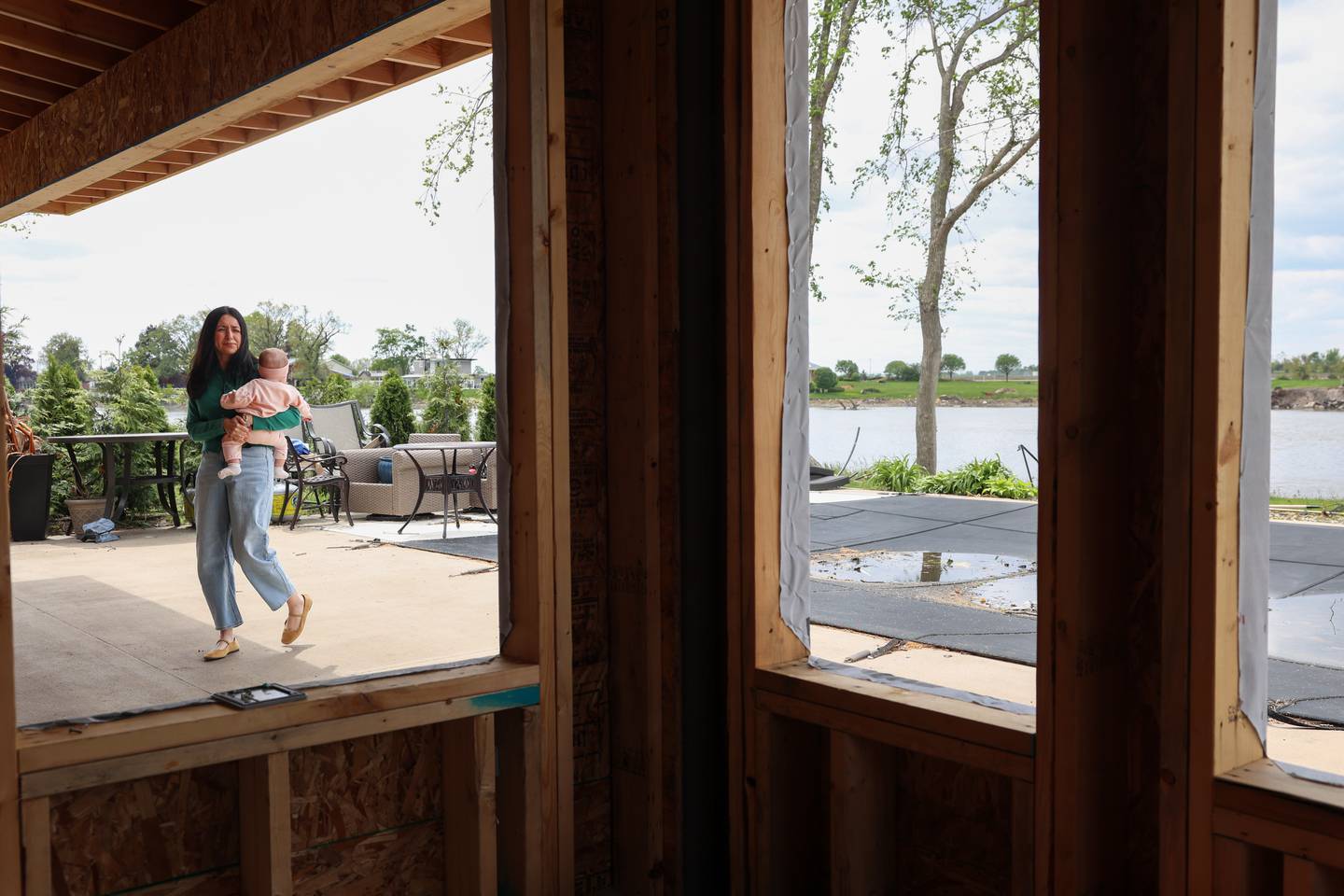 Anabel Horchem walks with her 5-month-old daughter, Amelia, around the back of their Aroma Township home on May 6, 2026. The windows of the backroom were destroyed in the March 10 tornado as Anabel sheltered with her daughter and husband, Jimmy, inside the bathroom tub.