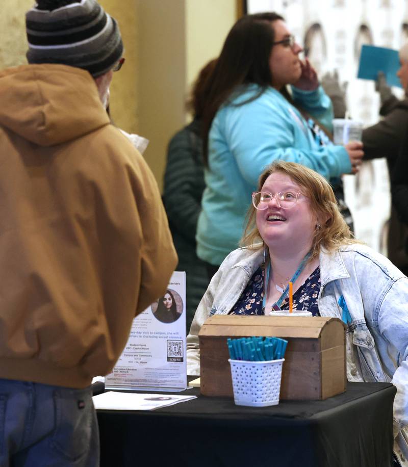 Shayna Smith, prevention educator with Safe Passage, greets a visitor Monday, April 7, 2025, during the Safe Passage Take Back the Night and Survivor Speak Out at the Egyptian Theatre in Dekalb. The event is held in conjunction with Sexual Assault Awareness Month.