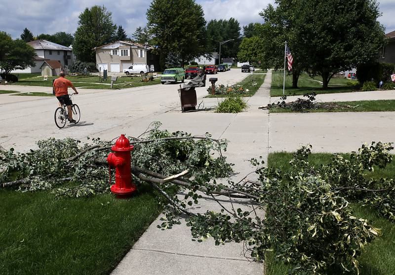 A man rides his bicycle past debris lining the road in the 10700 block of Timer Drive West in Huntley on Thursday, July 13, 2023, after a confirmed tornado took the roof off the building in Huntley on Wednesday.