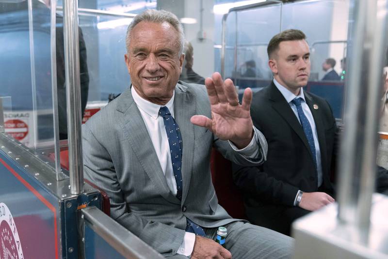 FILE - Robert F. Kennedy Jr., waves to reporters as he rides the train to go to meet with Sen. John Thune, R-S.D. at the Capitol in Washington, Dec. 17, 2024. (AP Photo/Jose Luis Magana, File)