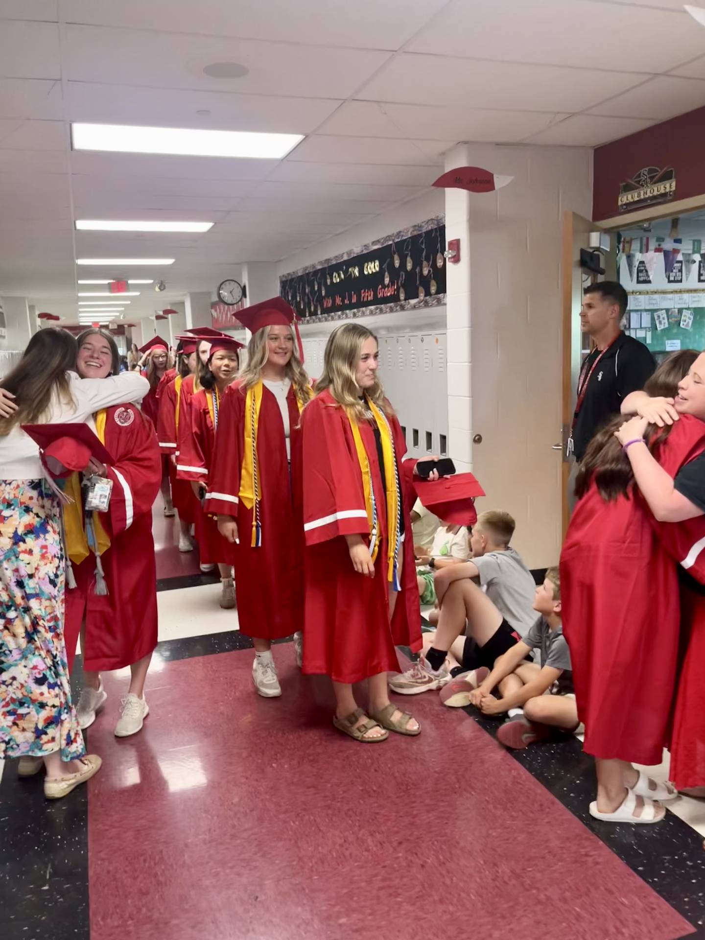 Graduating Yorkville High School seniors stop to embrace former teachers at Grande Reserve Elementary School as younger students applaud their accomplishment.