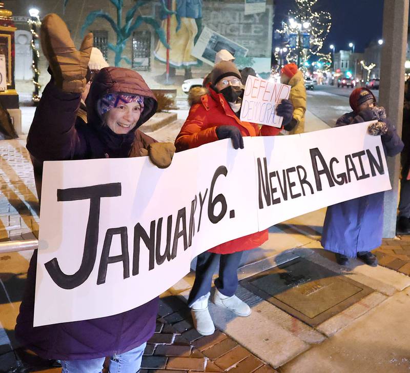 Cynthia De Seife, (left) a member of Responsive Engagement Activating Civic Talent, along with other demonstrators wave at passing cars Friday, Jan. 6, 2023, during a Stand for Democracy demonstration at Memorial Park in downtown DeKalb. The second annual event was held to affirm the attendees commitment to American democracy.
