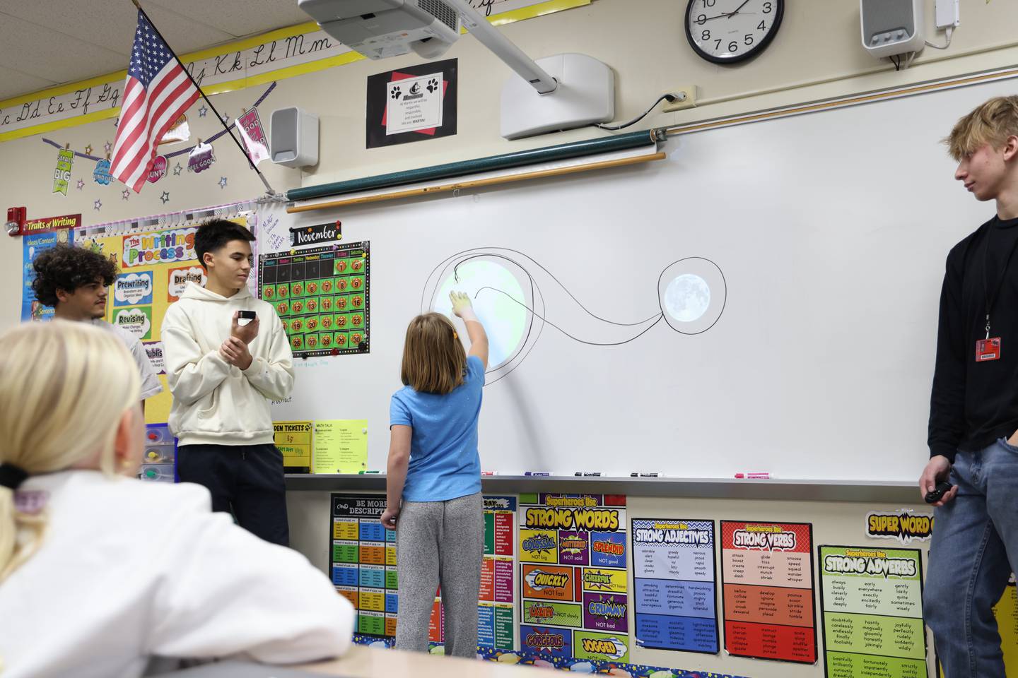 A third grader draws a projected flight path for the Artemis II space mission on a whiteboard during a presentation at Martin Elementary School Nov. 14 by Huntley High School students about their NASA app challenge project. Also pictured Huntley High students Kerellos Abdelmalak, Allen Williams and Daniel Przybylko.