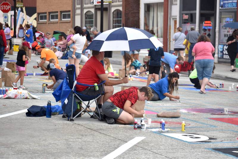 Even with occasional rain showers on Saturday the 25th annual Paint the Town was held in downtown Morrison. Each participant received a bag filled with five primary colors, paint brushes, chalk for sketching, a palette to mix paint, color mixing instructions, hand wipes, and an event t-shirt and giveaways from sponsors. Despite the impending rain, the artists worked away to fill their five-foot squares to create an original work of art.