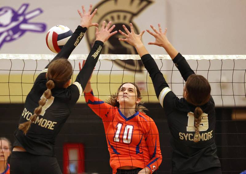 Genoa-Kingston's Rylie Stoffregen tries to tip the ball by two Sycamore blockers during their match Monday, Aug. 28, 2023, at Sycamore High School.