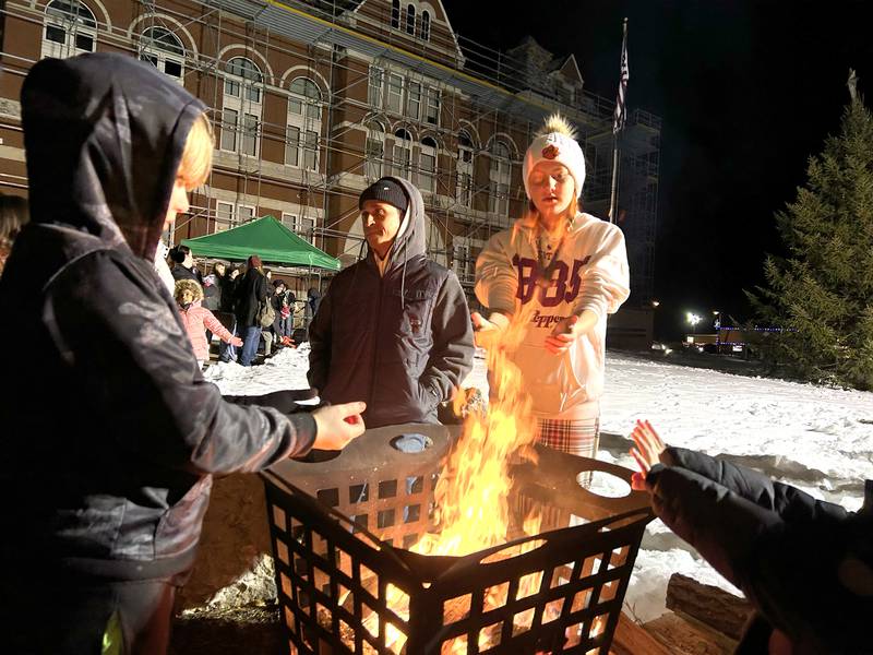 Visitors to Oregon's Candlelight Walk on Saturday, Dec. 6, 2025 warm their hands at one of the fire pots as they wait for the lighting of the Christmas tree on the Ogle County Courthouse lawn.