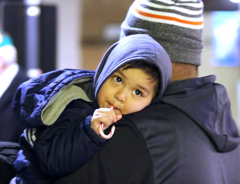 Mateo Mendez, 2, from DeKalb, enjoys a candy cane as he waits patiently with his dad Jose for Santa's arrival to light the tree Thursday, Dec. 2, 2021, during Lights on Lincoln and Santa Comes to Town.