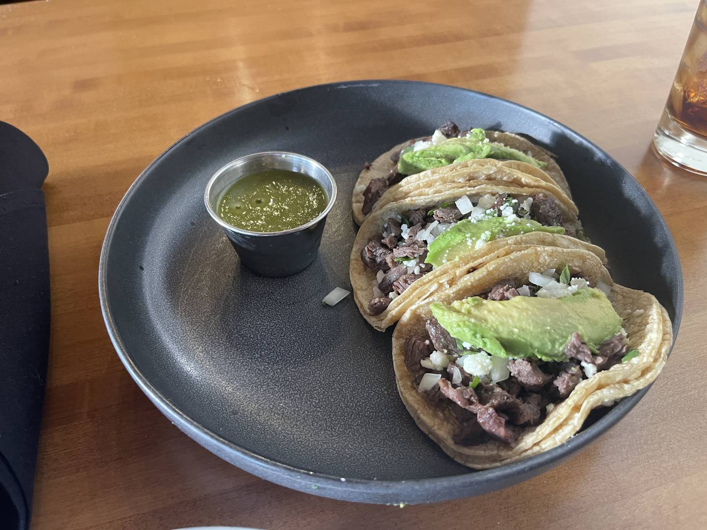 Grass fed sirloin steak street tacos with avocado, onion, queso fresco, cilantro with a side of salsa verde, on a corn tortilla.