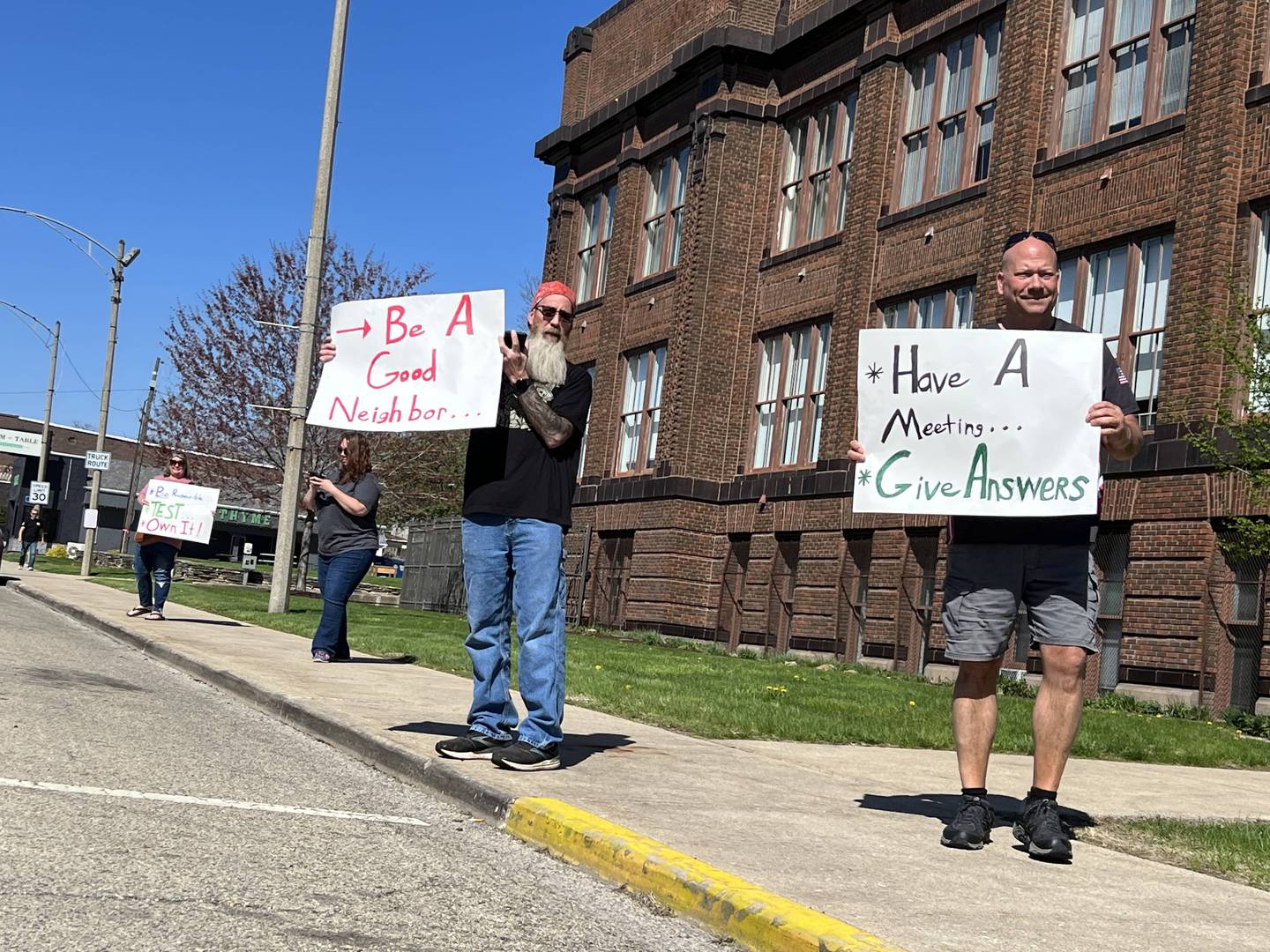 La Salle Mayor Jeff Grove (right) and resident Jamie Hicks hold protest signs Wednesday, April 12, 2023, in front of Carus headquarters in Peru.
