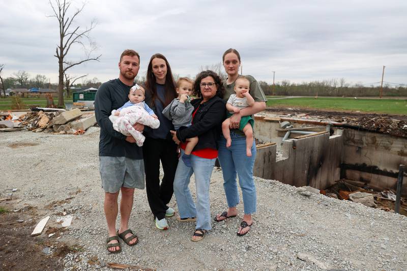 Lisa Gerth, second adult from right, stands with her son and daughter-in-law, Mitchell and Abigail Gerth, at left, with their children Everett, almost 2, and Elowyn, 4 months, as well as close friend and neighbor Erin Boerschig, right, and her 8-month-old son Sawyer, on April 15, 2026, outside the basement where they sheltered during the March 10 tornado that hit Aroma Township.