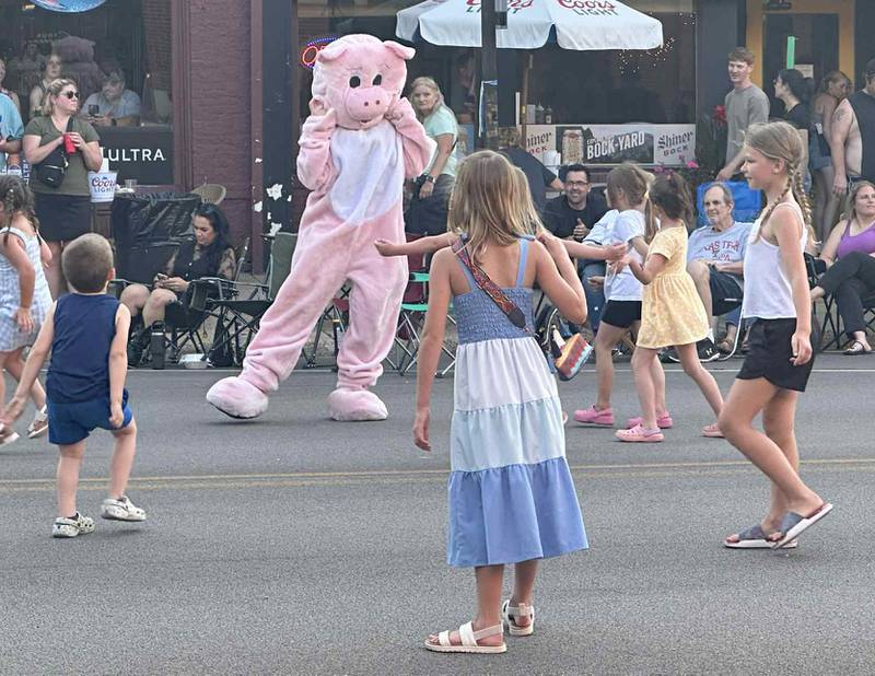 A pig mascot dances to the music with children during the "Down on Main Street" concert featuring Mae Estes on Friday, June 20, 2025 downtown Princeton.